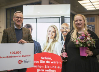 Hans-Martin Rump, Leiter der Agentur für Arbeit Kiel, überreicht der Kundin einen Blumenstrauß und eine Flasche alkoholfreien Rosmarin-Prosecco.