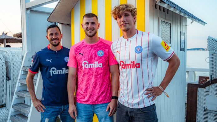 Holstein Kiel Trikots 2026/27 Holstein Kiel Trikots 2026/27 v. li.: Steven Skrzybski im Heimtrikot, Timon Weiner im Torwartjersey und Lasse Rosenboom