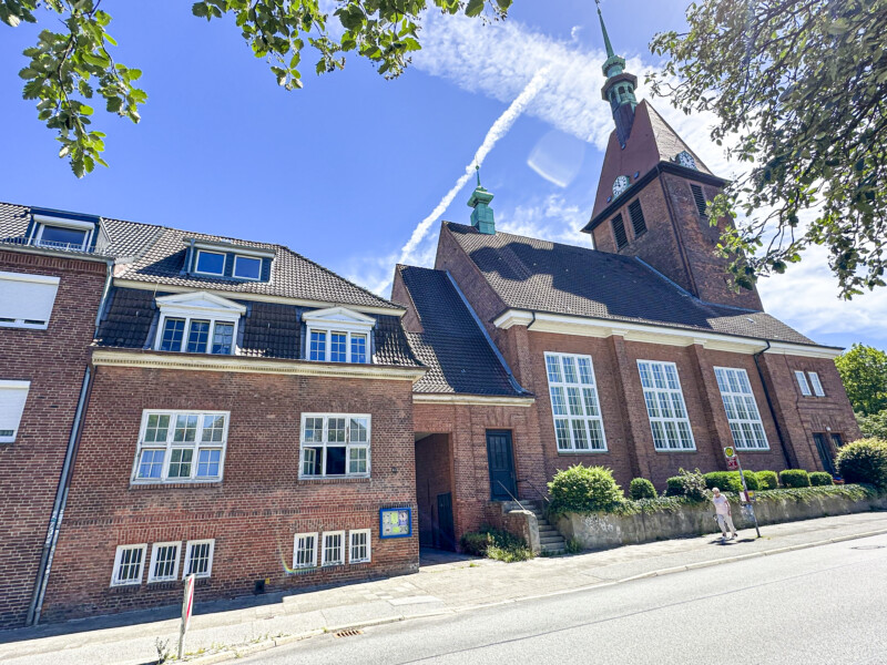 Michaeliskirche Hassee Gemeindezentrum: Straßenansicht des neuen Gemeindezentrums am Wulfsbrook. Links das alte Küsterhaus aus dem Jahr 1911. Es ist sanierungsbedürtig und wird im ersten von drei Bauabschnitten energetisch saniert. Rechts daneben die Michaeliskirche, in deren Seitenschiff der Versammlungsraum reaktiviert werden soll. Im zweiten Bauabschnitt entsteht dort der neue Gemeindesaal.