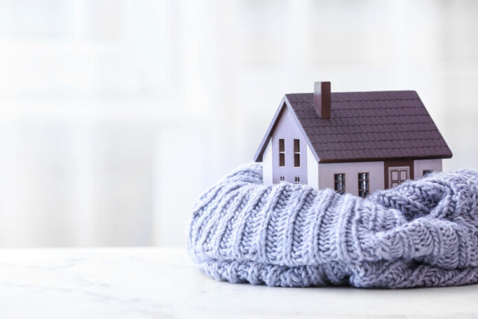Figure of house and warm scarf on table. Concept of heating season Figure of house and warm scarf on table. Concept of heating season